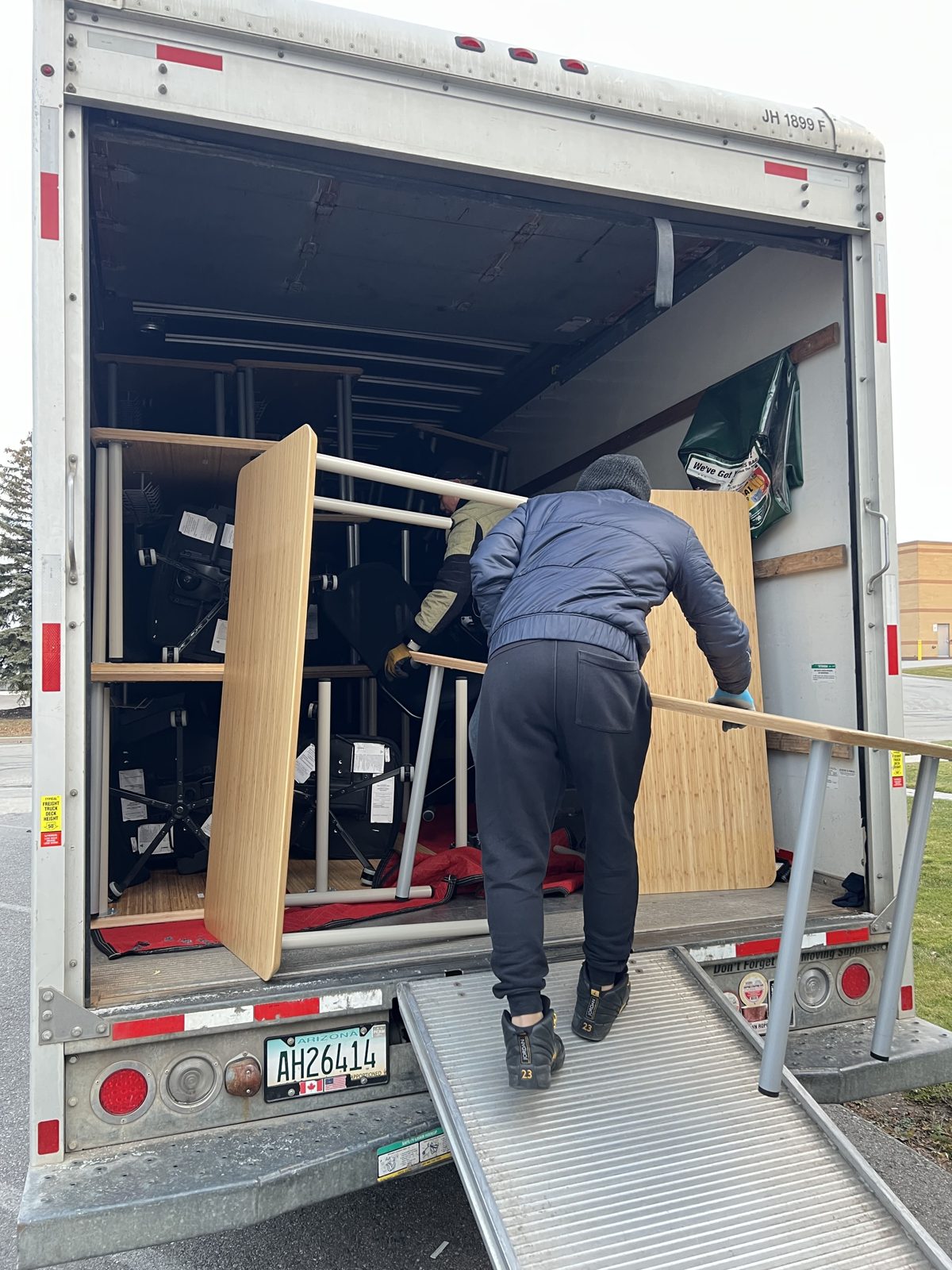 Mover loading a disassembled office desk into the moving truck up a ramp