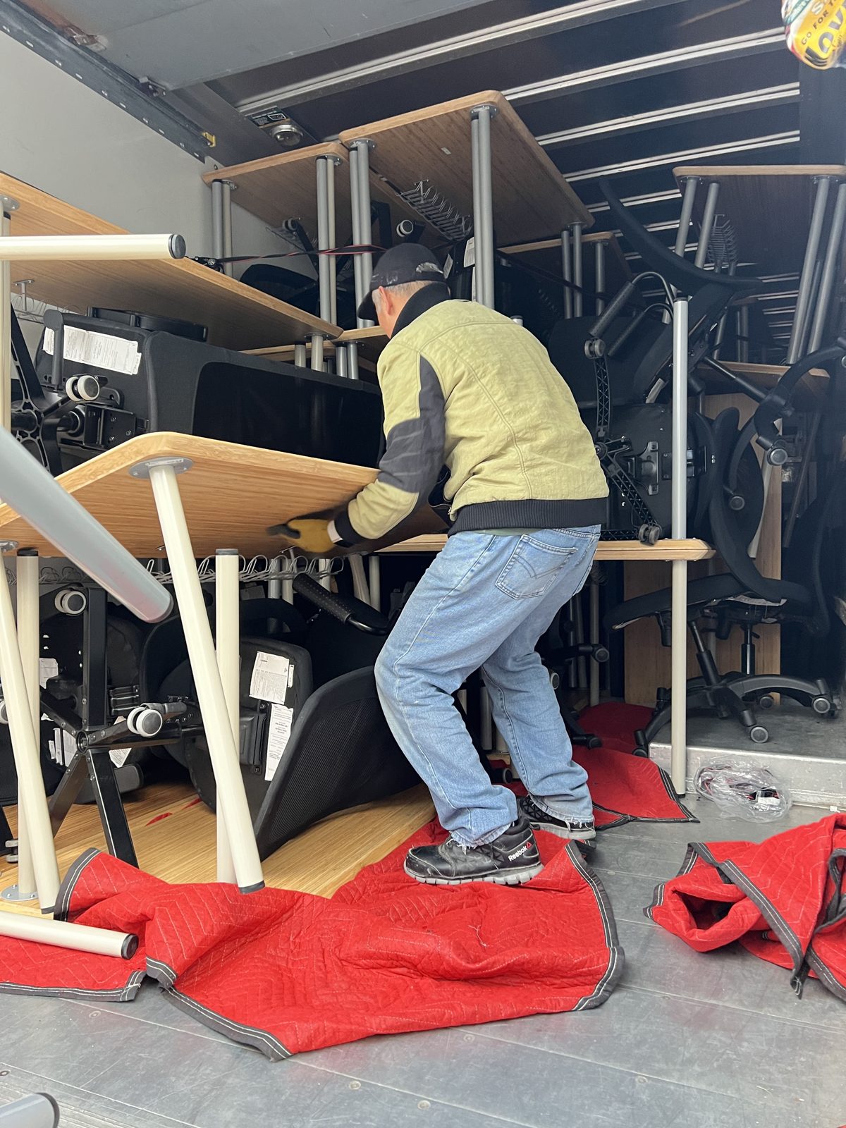 Mover strapping office desks and chairs against the wall inside a moving truck