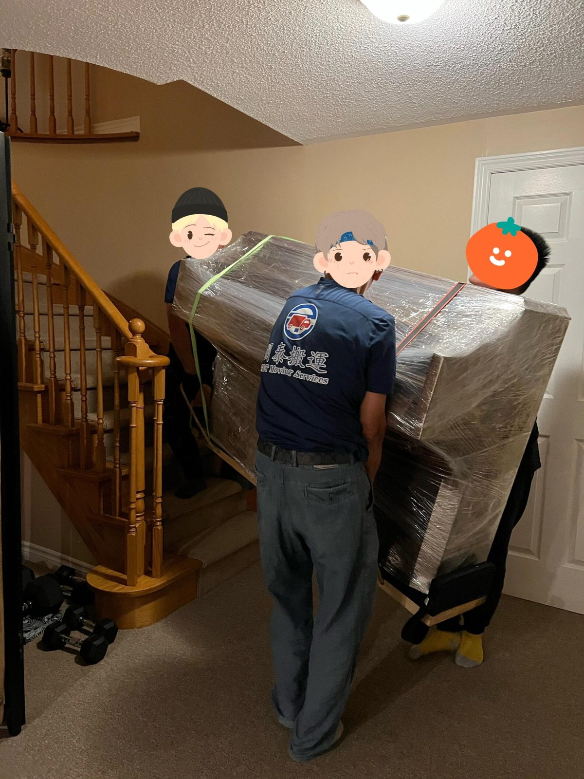 Three G&T movers carrying a shrink-wrapped upright piano up a curved basement staircase
