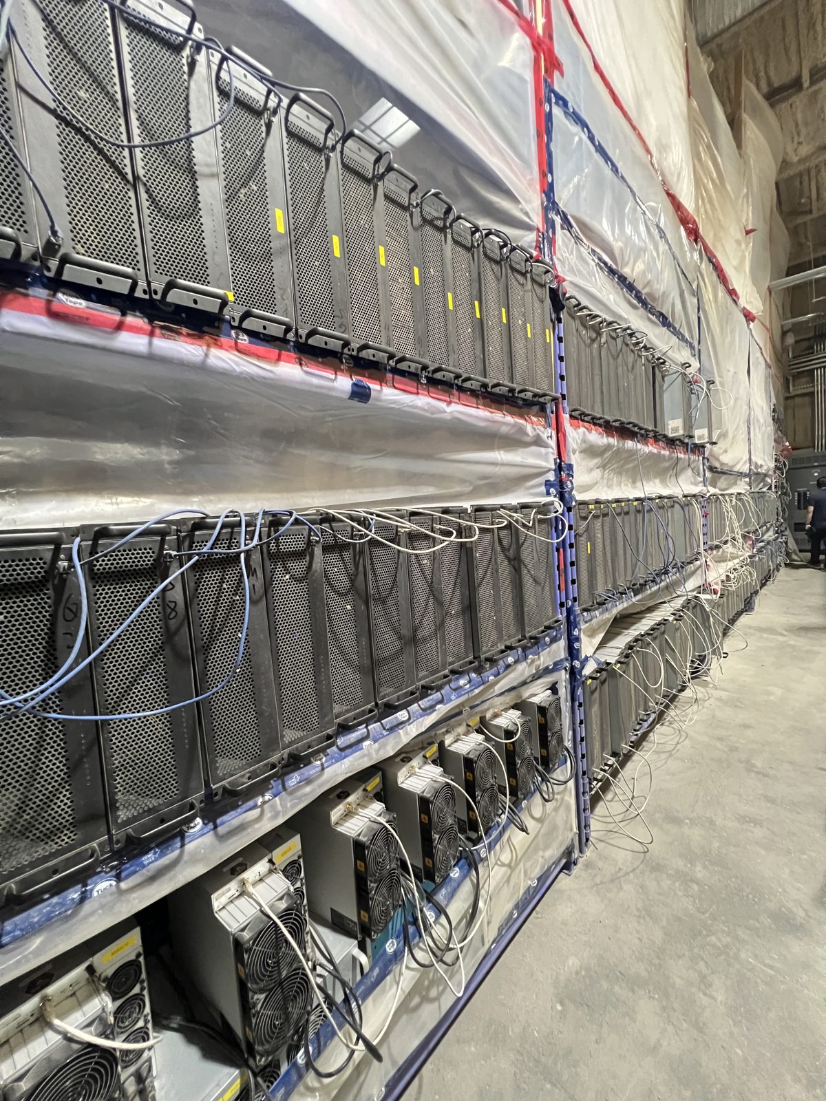 Rows of racked server and mining units with cabling installed in a warehouse